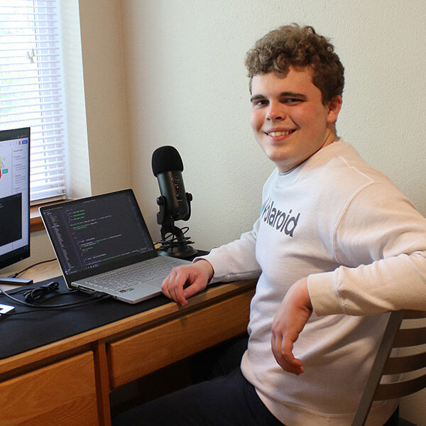 Computer Science student Sam Jennings sitting at a desk in front of a computer and monitor