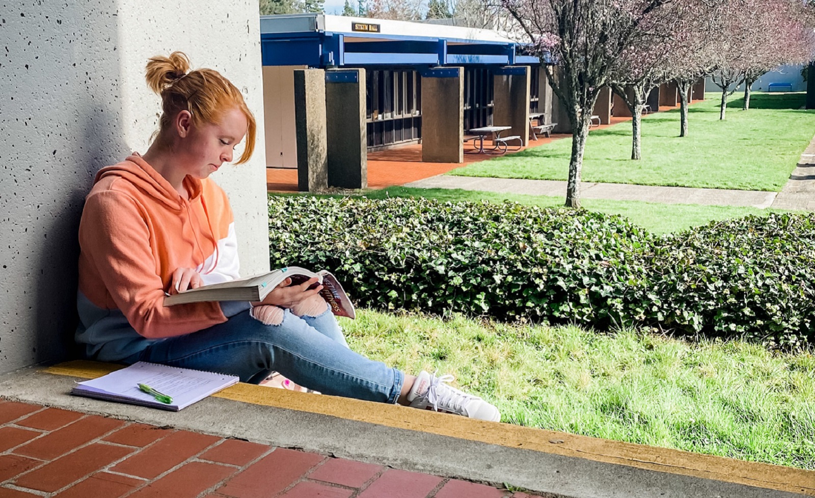 Photo of female student reading a book outside on SWOCC's Coos Campus