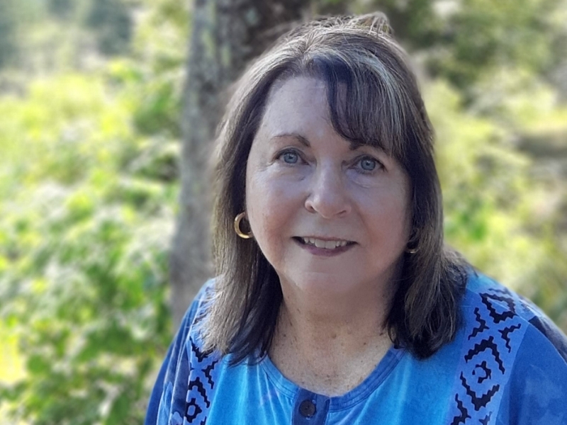 Woman looking into camera with green trees and leaves in background